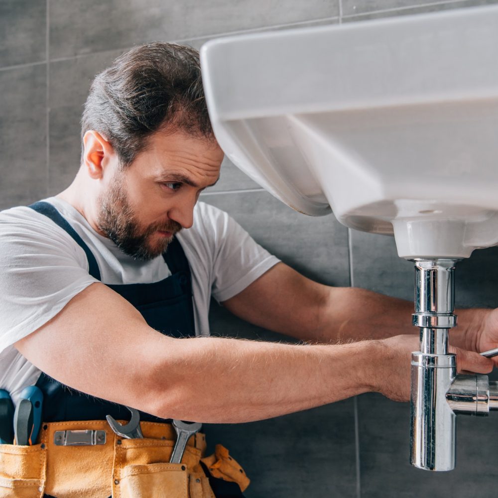focused-male-plumber-in-working-overall-fixing-sink-in-bathroom.jpg focused-male-plumber-in-working-overall-fixing-sink-in-bathroom.jpg